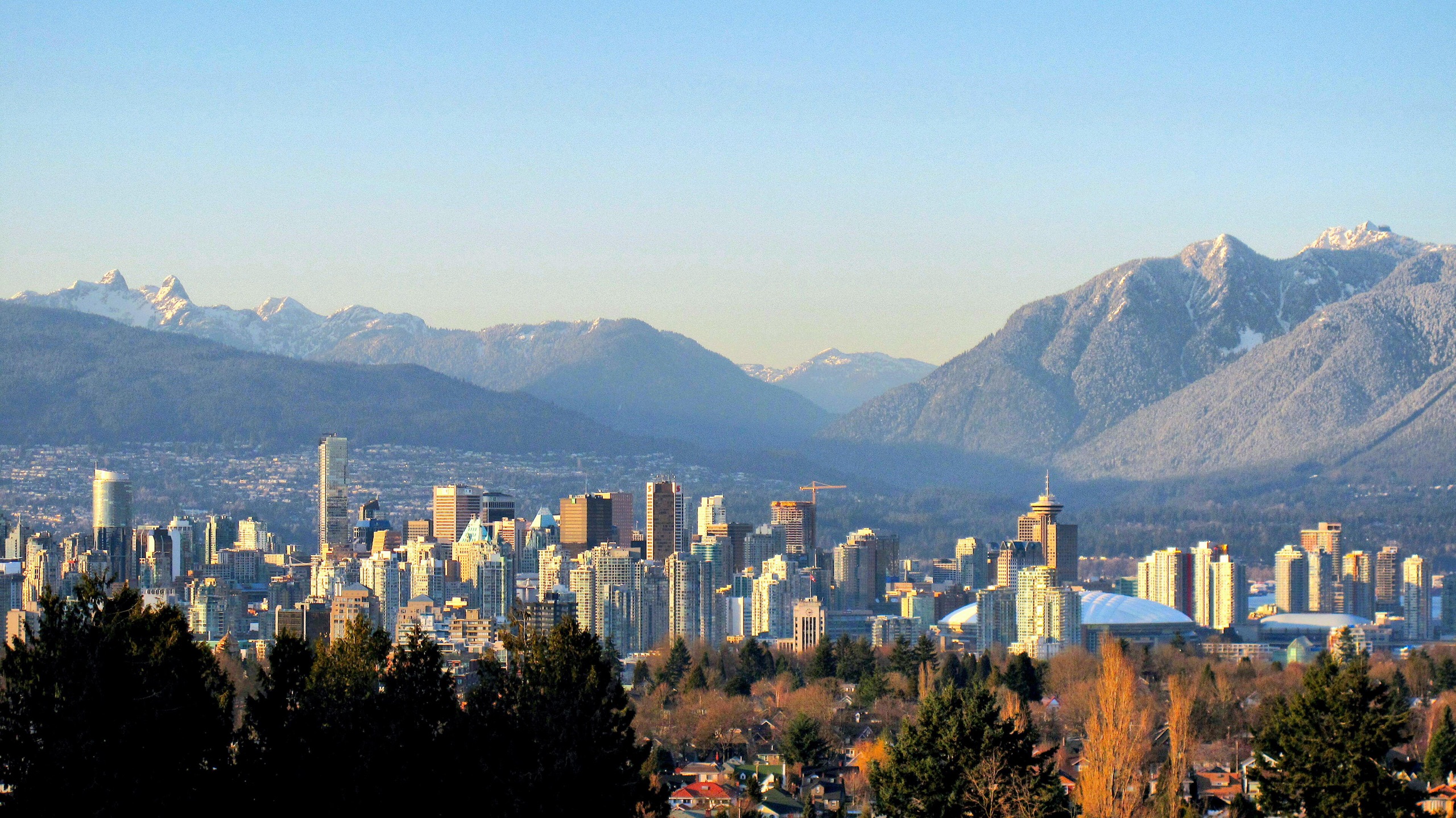 Downtown Vancouver in late-afternoon sun, the snow-capped North Shore mountains behind